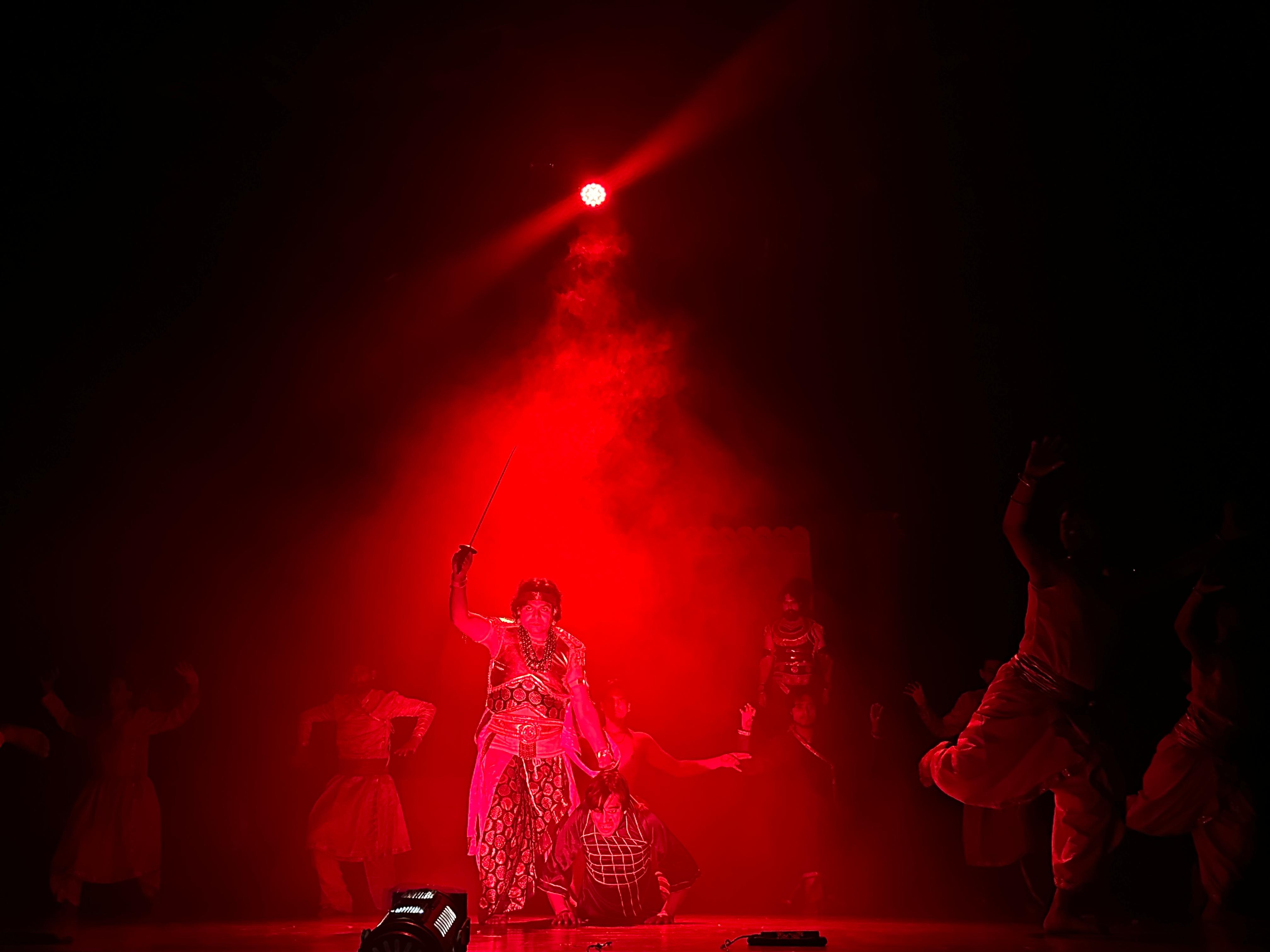 Ensemble scene with a raised sword under red lighting