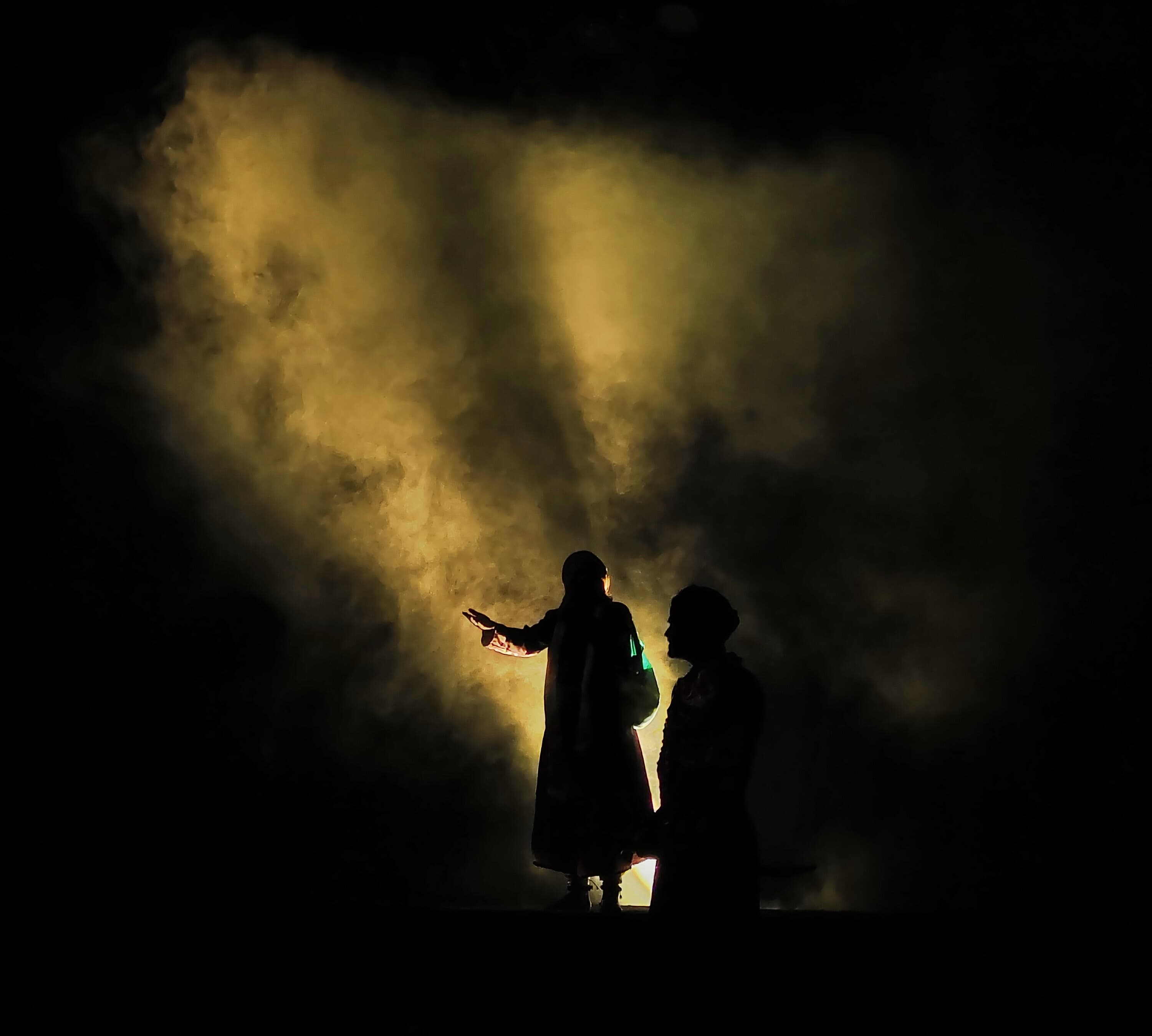 Silhouetted performers surrounded by golden stage smoke