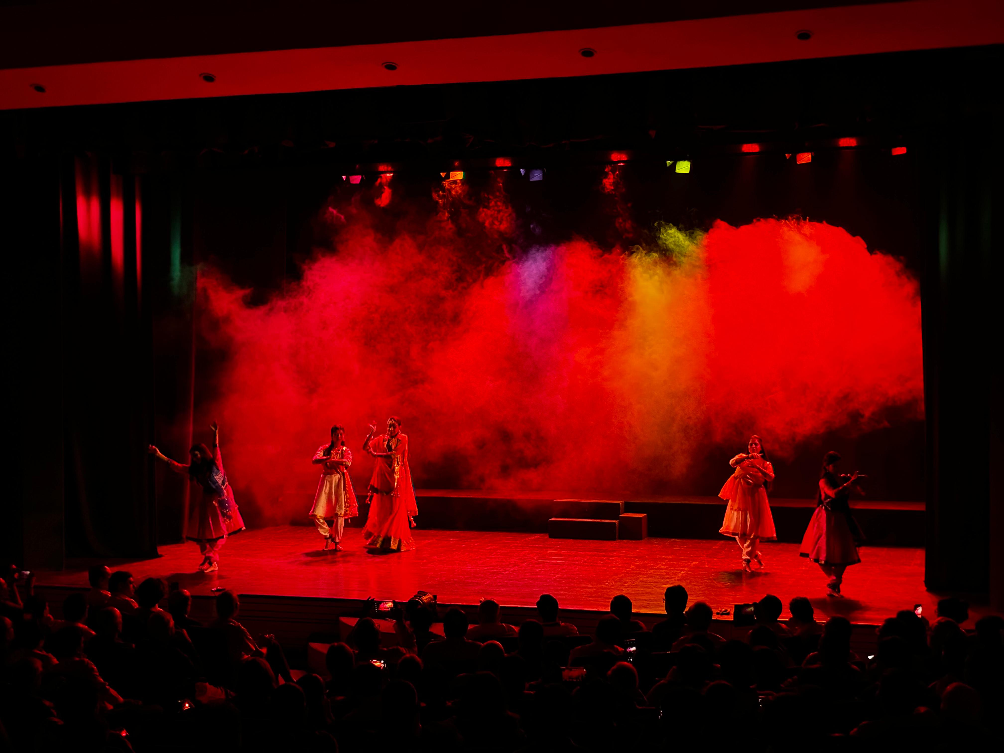 Dancers performing beneath red lighting and stage smoke