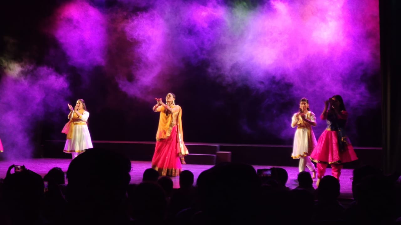 Performers dancing beneath purple stage lighting