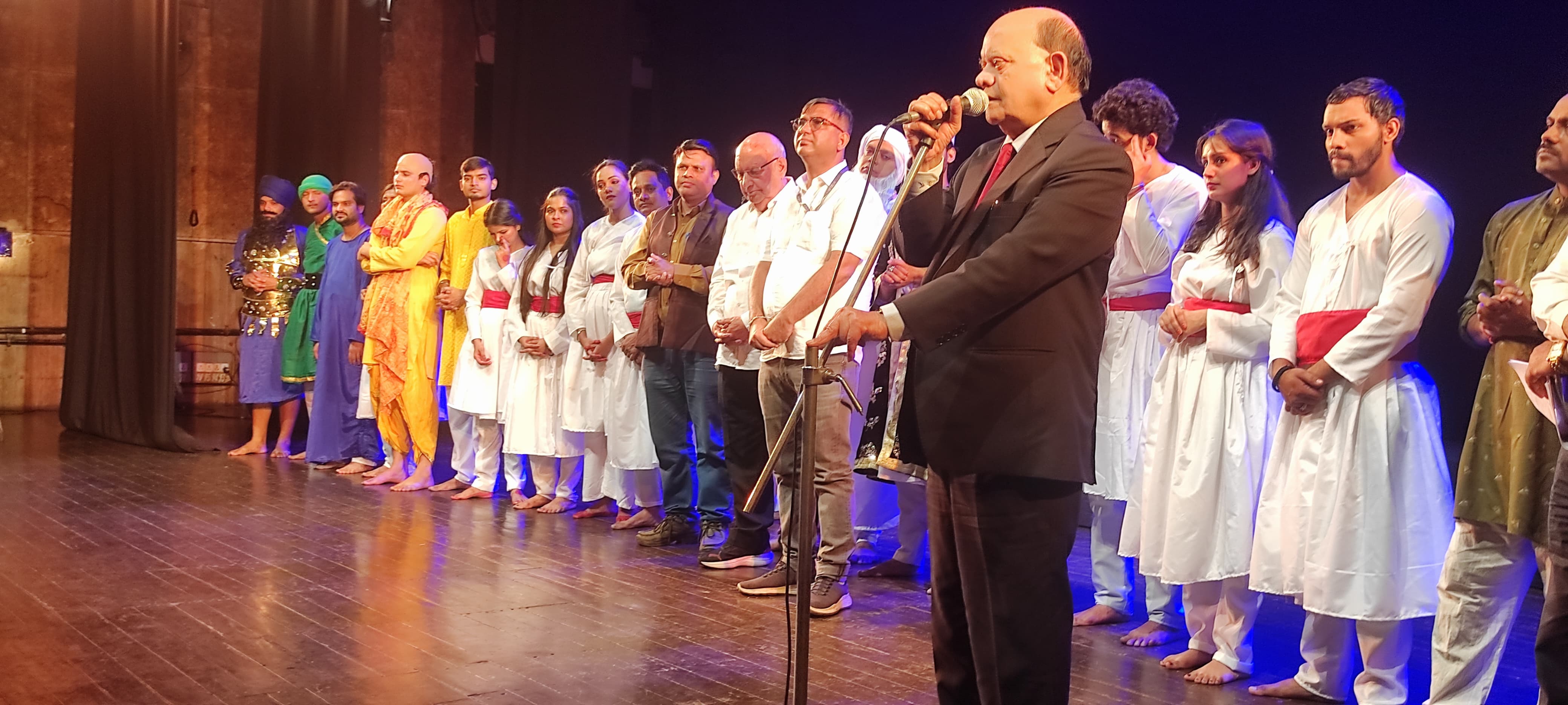 Speaker addressing the audience with cast and guests on stage