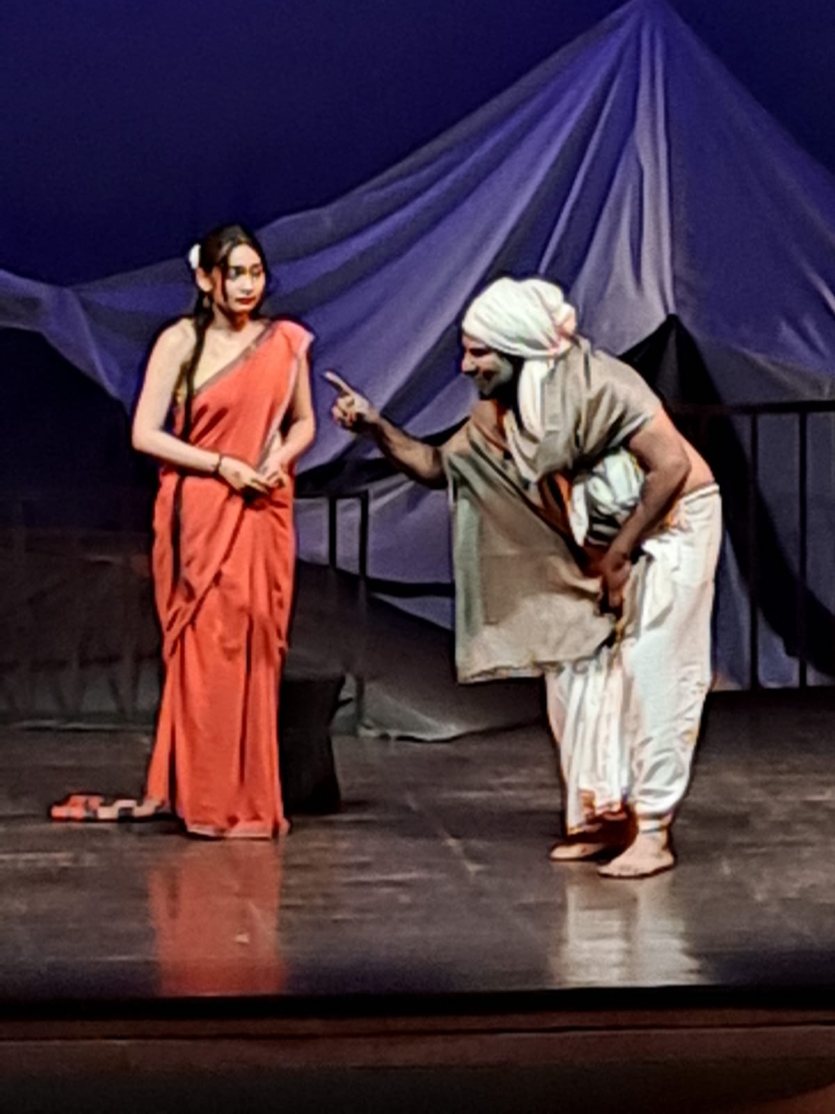 Two actors in a scene beside draped mountain scenery